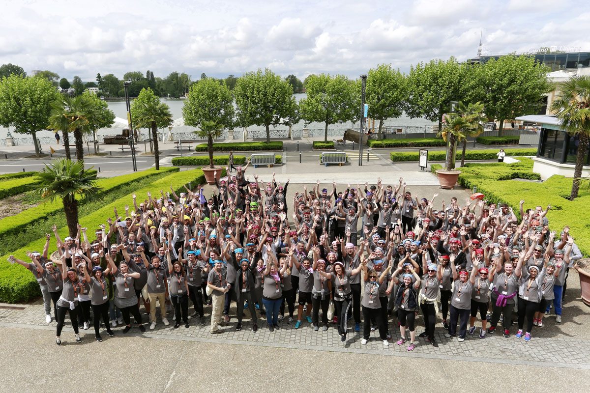 Grand groupe de collaborateurs, bras levés, lors d'un team building en extérieur