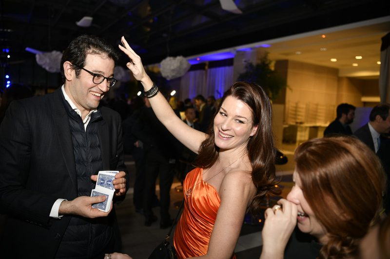 Magicienne en robe orange et un invité tenant un jeu de cartes lors d'une soirée d'entreprise