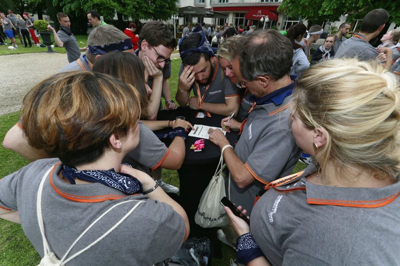 Équipe en polos gris et bandanas réunie autour d'une table pour résoudre une épreuve lors d'un team building en extérieur